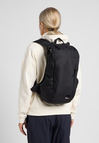 Black fabric backpack with a sleek design, featuring adjustable straps, a front zip pocket, and brand logo at the bottom front.