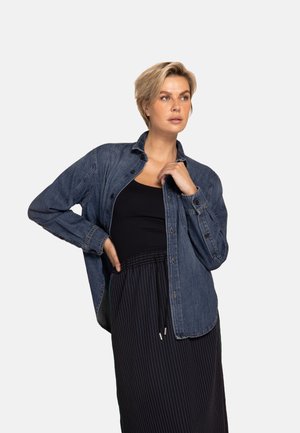Denim shirt in dark blue with a collar, front buttons, and long sleeves. Paired with a black tank top and striped skirt.