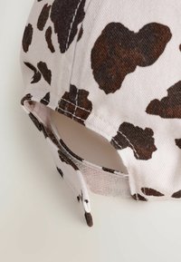 Cap mit einem hellbeigen Stoff und braunen, leopardähnlichen Flecken, einem verstellbaren Riemen und sichtbaren Nähakzenten.