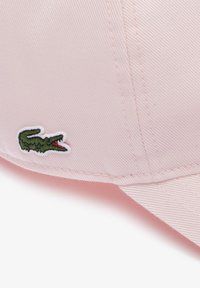 Casquette rose en tissu texturé, avec une visière courbée et un logo de crocodile vert brodé sur le côté.