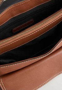 Borsa a tracolla in pelle marrone con superficie testurizzata, dotata di chiusura con zip, foderata in nero e con una tasca interna. Dettagli cuciti lungo i bordi.