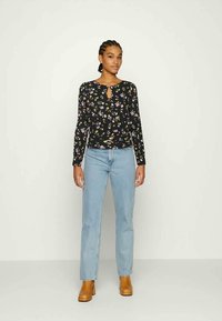 Top preto de manga longa com estampado floral, apresentando um decote em forma de buraco de chave, combinado com jeans de perna reta azul claro e botas de tornozelo castanhas.