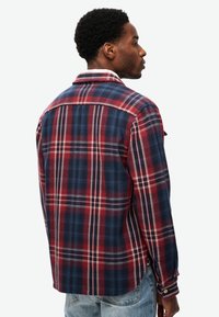 Blauw en rood geruite blouse met kraag, lange mouwen en een afgeronde zoom. Bevat witte accentlijnen en knoopmanchetten.