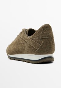 Brown suede sneaker with a textured finish, rounded shape, white midsole, and a black rubber outsole featuring small traction patterns.