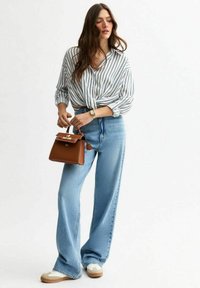 Leichte, gestreifte Hemdbluse, am Bund gebunden; weite blaue Jeans; kleine braune Handtasche mit goldenen Akzenten; weiße Sneakers.