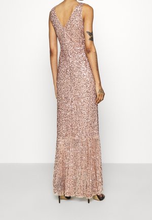 Mujer vestida con un vestido rosa de lentejuelas sin mangas y largo hasta el suelo, con un escote en V profundo en la espalda, de pie con las manos relajadas a los costados.