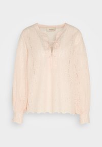 Blouse rose pâle à manches longues avec motif en dentelle ajourée, ourlet et poignets festonnés, et fermeture à nouer à l'avant au niveau du col rond.