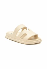Sandalia beige tipo zueco con dos correas anchas, detalles recortados, textura suave y una suela baja y flexible.