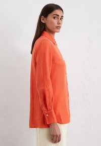 Camicia arancione in lino con collo e maniche lunghe. Presenta una vestibilità comoda e dettagli di bottoni discreti.