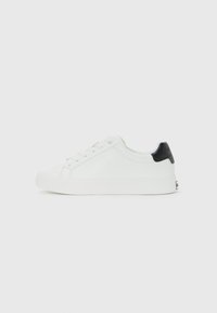 Sneaker bassa bianca con lacci davanti e tab nera sul tallone, design minimal su sfondo bianco uniforme.