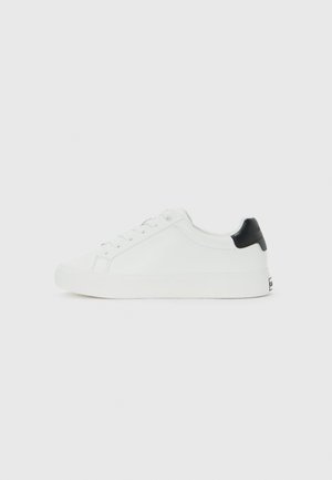 Zapatilla baja blanca con cordones en la parte delantera y una pestaña negra en el talón, diseño minimalista sobre un fondo blanco liso.