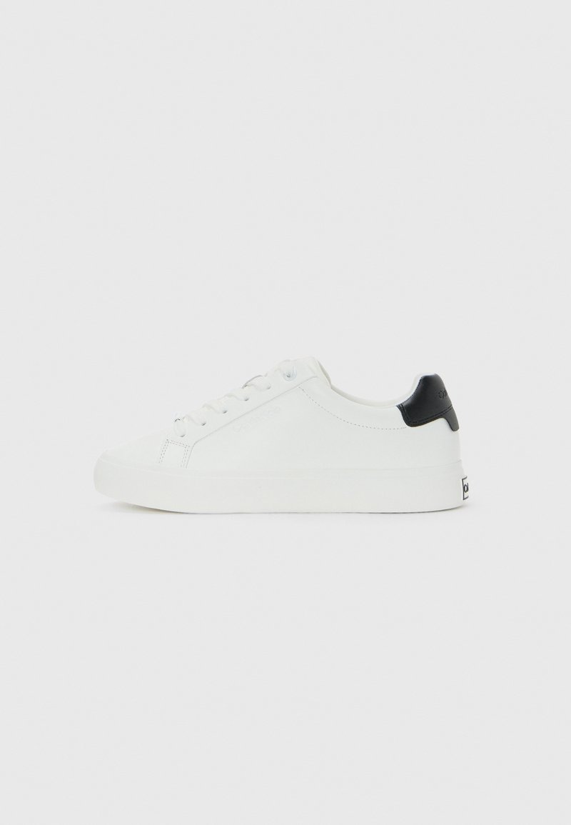 Sneaker bassa bianca con lacci davanti e tab nera sul tallone, design minimal su sfondo bianco uniforme.
