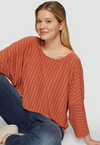 Roodbruine gestreepte top met ruime mouwen en een ronde halslijn, voorzien van een gestructureerd stofontwerp en een ontspannen pasvorm. Casual look gecombineerd met blauwe jeans.