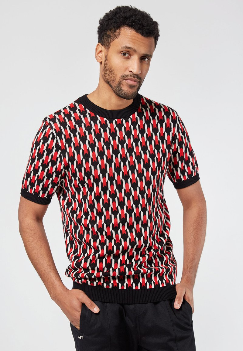 Suéter de punto de manga corta con un patrón geométrico en rojo, blanco y negro. Cuello y puños acanalados. Textura suave, diseño ajustado.