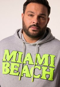 Felpa grigia con grande scritta pelosa "MIAMI BEACH" in verde neon, con cappuccio regolabile e un tessuto morbido.