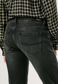 Mustmustest denim püksid, millel on sobiv siluett, kahe tagatasku ja peente õmblusdetailidega, kanda koos ruudulise särgiga.