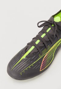 Grå fotballsko med teksturert overflate, med neon grønn og rosa detaljer, strømlinjeformet design og tett snøring.