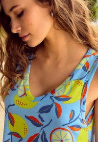 Haut sans manches bleu avec un motif de fruits et de feuilles vibrant en vert, jaune, orange et rouge, doté d'un col rond et d'un tissu doux.
