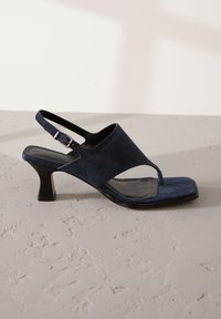 Sandale slingback en daim bleu marine avec un bout carré, dotée d'un petit talon et d'une unique boucle sur la bride. Texture lisse sur toute la surface.