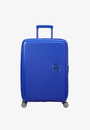 Valigia rigida blu con design testurizzato circolare, manico retrattile e quattro ruote. Presenta un logo del marchio argentato sul fronte.