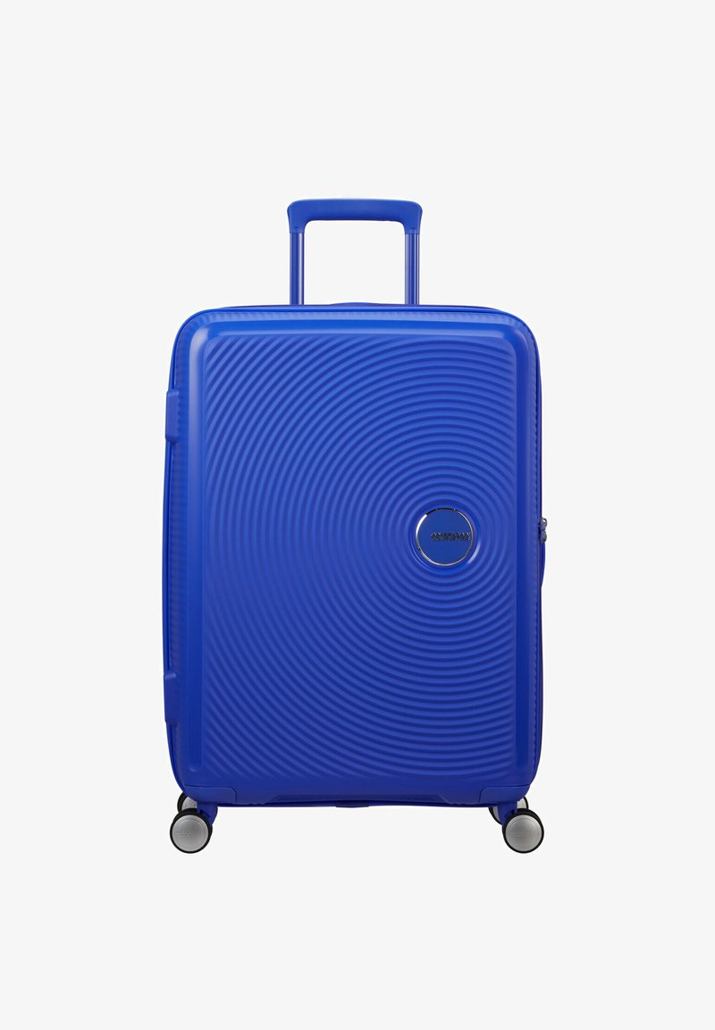Valigia rigida blu con design testurizzato circolare, manico retrattile e quattro ruote. Presenta un logo del marchio argentato sul fronte.