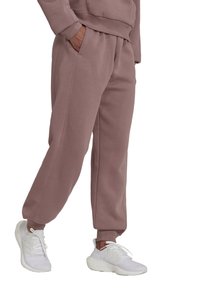 Licht mauve sweatpants met een elastische tailleband, zijzakken en ribbelboorden, gecombineerd met witte sportschoenen. Zachte stoftextuur.