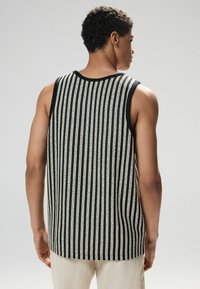 Ärmelloses, gestreiftes Tanktop in Schwarz und Creme, mit einer Strickstruktur und einem runden Ausschnitt sowie einem gerippten Saum.