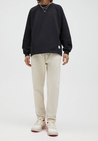 Tmavě námořnická mikina s raglánovými rukávy, doplněná světle béžovými kalhotami a bílými teniskami s červenými detaily. Jednoduchý design, ležérní střih.