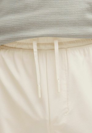 Pantalones jogger de corte holgado y color crema, con una cinturilla elástica y cordón ajustable. Tela suave con textura lisa y bolsillos laterales.