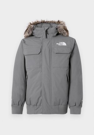 Graue isolierte Jacke mit abnehmbarer Kapuze und Kunstpelzbesatz, zwei Brusttaschen und elastischen Bündchen. Das Logo ist auf der Brust angebracht.