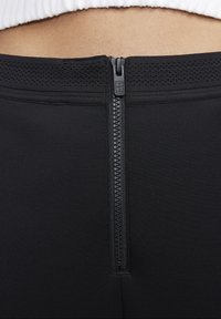 Svarta leggings i syntetiskt material med en mjuk textur, detalj med en central dragkedja på baksidan och ventilerande mesh-accenter.