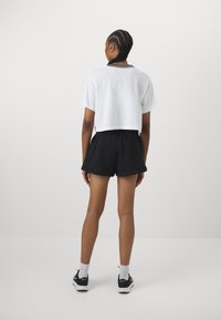 T-shirt branca oversized com bordas pretas, combinada com calções pretos de cintura elástica. O modelo usa meias brancas e ténis pretos.