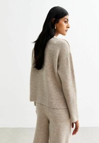 Pull en maille beige avec une coupe décontractée et des épaules tombantes, associé à un pantalon beige assorti. Texture douce, design minimal, longueur raccourcie.