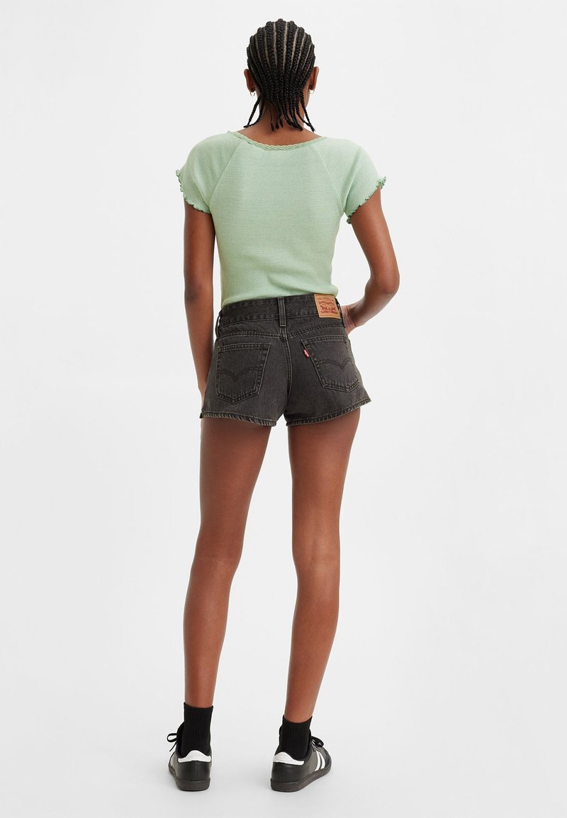 Top corto de color verde menta con textura acanalada y bordes en forma de onda, combinado con pantalones cortos de mezclilla negros de cintura alta y zapatillas negras.