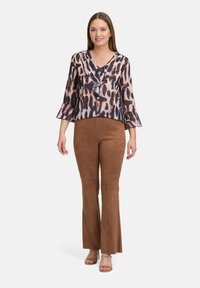 Blouse transparente avec un col froncé dans un imprimé animal beige et marron, associée à un pantalon évasé beige clair en matériau doux.