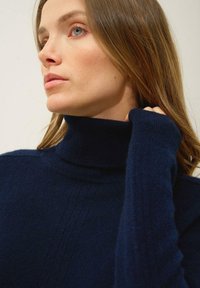 Granatowy sweter z golfem wykonany z miękkiej dzianiny, z wyraźną teksturą ściągacza oraz subtelnymi pionowymi liniami na klatce piersiowej.