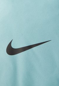 Turkist Nike-stof med en struktureret vævning, der har et fremtrædende sort swoosh-logo. Fokus på materialer og designelementer.