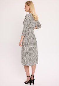 Czarna i biała midi sukienka w wzory z długimi rękawami i dopasowanym talią. Noszona z czarnymi sandałami na wysokim obcasie.