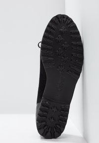 Chaussures noires avec une semelle en caoutchouc texturée. Tige en suède noir avec un accent lisse noir autour du talon.