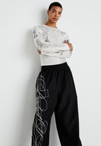 Long-sleeve white top with black illustrations; black pants with white cursive text and abstract lines; relaxed fit; soft textures.
