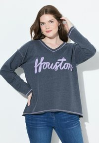 Maglietta a maniche lunghe grigio scuro con scollatura a V, caratterizzata dalla scritta "Houston" in corsivo viola chiaro. Le cuciture distintive ai polsini e all'orlo aggiungono contrasto.