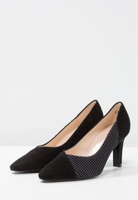 Zapatos de tacón alto negros con punta afilada, que presentan una combinación de ante y tejido texturizado. Tacón negro brillante y forro interior suave.