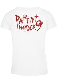 T-shirt en coton blanc avec un texte rouge éclaboussé au dos qui dit "NUMÉRO DE PATIENT 9" dans une police en gras et usée.