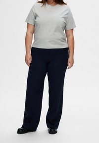 Graues kurzärmliges T-Shirt, kombiniert mit navyfarbenen weiten Hosen, ergänzt durch schwarze Fußbekleidung. Schlichtes Design ohne sichtbare Muster oder Akzente.