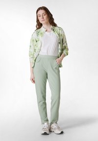 Lichte bloemrijke zip-up jas in groen met witte accenten, in combinatie met zachte mintgroene broek met zijzakken. Lichte sneakers.
