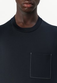Camiseta de manga corta en color navy, confeccionada en un tejido suave, con cuello redondo y un bolsillo rectangular en el pecho con un detalle de costura en contraste.