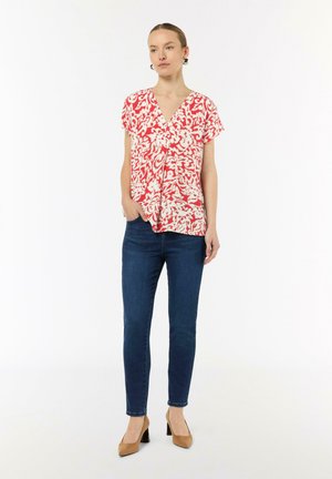 Red and white patterned blouse with a V-neck, short sleeves, and a relaxed fit, paired with dark blue skinny jeans and beige heels.