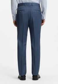 Ciemnoniebieskie spodnie w prążki o dopasowanym kroju, z dwoma tylnymi kieszeniami zapinanymi na guziki, zestawione z jasną koszulą w paski.