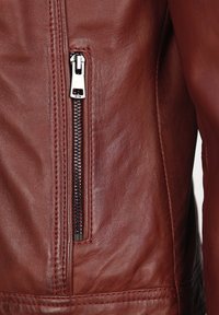 Bruine leren jas met een ritssluiting aan de zijkant, met contrasterende rode stiksels en een zachte textuur. Close-up van het ritssluitingdetail.