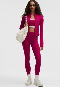 Kere roosa sportlik jakk, lühike särk ja retuusid; tekstureeritud kangas; koos valge nöörikott ja heledate spordijalatsitega.